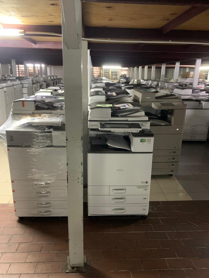 Warehouse aisle lined with wrapped and unwrapped copiers ready for delivery